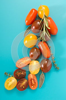 Colorful cherry tomatoes cluster with herbs, on blue background.