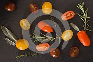 Colorful cherry tomatoes with herbs, on black