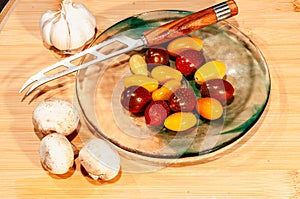 Colorful cherry tomatoes, knife on blue, glass plate and, garlic clove and mushrooms, around plate