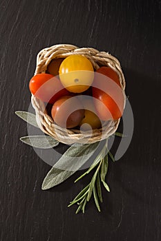 Colorful cherry tomatoes in wicker basket with herbs