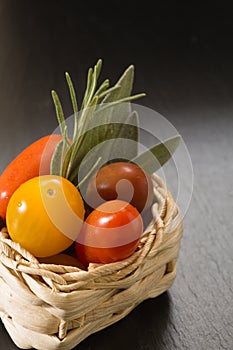 Colorful cherry tomatoes in wicker basket with herbs