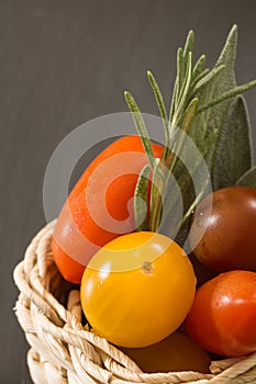 Colorful cherry tomatoes in wicker basket with herbs