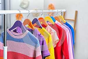 Colorful children`s clothes hanging on wardrobe rack indoors