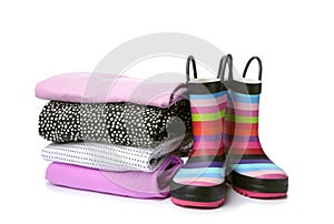 Colorful children`s rubber boots and stack of clothes