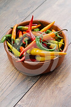 Colorful chili peppers in the ceramic bowl on a wooden table.