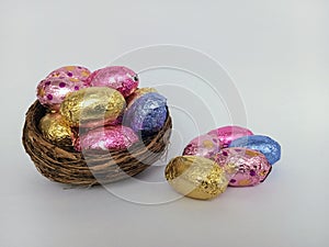 Colorful chocolate easter eggs overflowing a twig birds nest on a white background