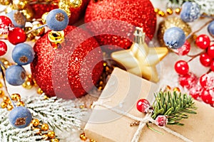 Colorful Christmas composition with gift, red baubles, holly berries, Xmas tree branch and golden garland on white snow background