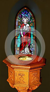 Colorful church window behind old wood baptismal font