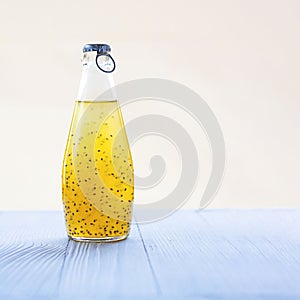 Colorful citrus refreshing summer drink with basil seeds in bottle with blue metal cap on light background. Square with