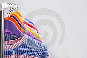 Colorful clothes hanging on wardrobe rack against light background, closeup.