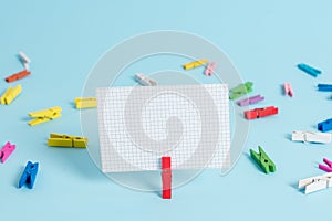 Colorful clothespin and rectangle square shaped colored paper in a blue background. Red clip hanging a note reminder in