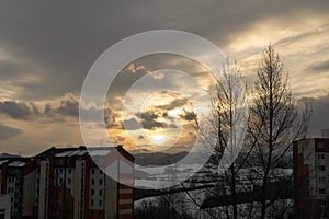 Barevné mraky nad městem a budovami nebo parkem a loukou, při východu nebo západu slunce.