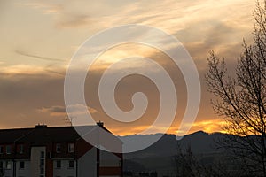 Barevné mraky nad městem a budovami nebo parkem a loukou, při východu nebo západu slunce.