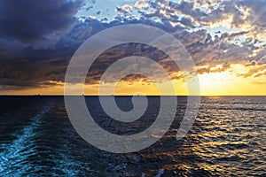 Cloudy sky above sea and wake from cruise ship at golden sunset