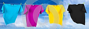 Colorful CMYK colored t-shirts on clothes line in front blue sky summer background. Cyan magenta yellow key symbol and printing