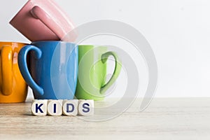 Colorful coffee mugs with a word `Kids` on white background on table