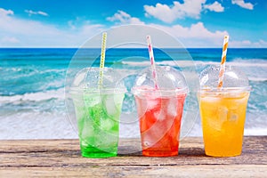 Colorful cold drinks in plastic cups on the beach