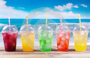 Colorful cold drinks in plastic cups on the beach