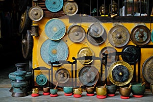 A colorful collection of ornamental gongs, sound bowls and buddha statues hanging on a yellow wall in a shop front in Hoi An,