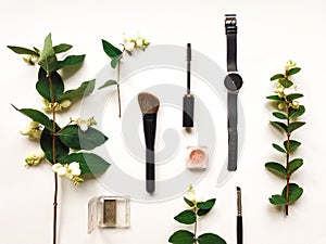 Colorful composition with woman make up tools and accessories, decorated with green snowberry branches. Flat lay on white table