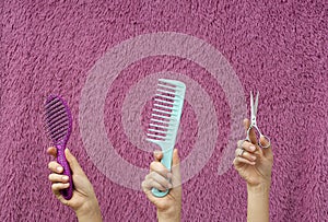 Colorful comsb,brush and scissors in women hands against pink hair background