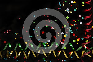 Colorful confetti and paper streamers on black background.