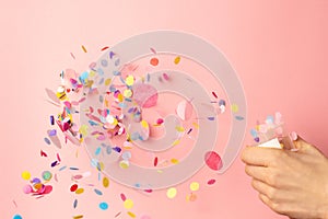 Colorful confetti in women`s hands on pastel pink background. Bright and festive holiday background
