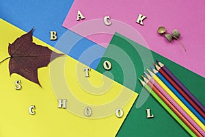 Colorful crayons, maple leaf and Back to school text, wooden letters on colored paper sheets. Concept of education