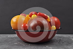 Variety of tomato cultivars in enamel bowl on concrete