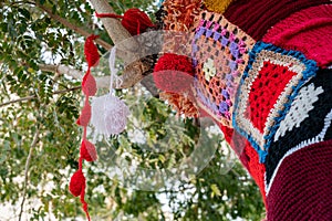Colorful crochet knit on a tree trunk yarn bombing. Patchwork knitted crochet covered tree for warmth, protection and