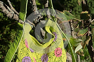 Colorful crocheted handbag with green handle behind the bush in the garden in summer