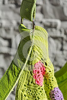 Colorful crocheted handbag with green handle behind the wall in the garden in summer