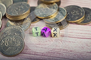 Colorful cube with word TAX and coins on wooden table