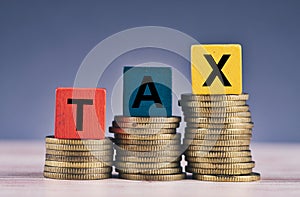 Colorful cube with word TAX and stacking coin on wooden table