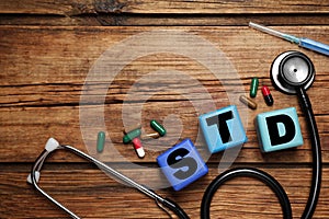 Colorful cubes with letters STD, capsules, stethoscope and syringe on wooden table, flat lay. Space for text