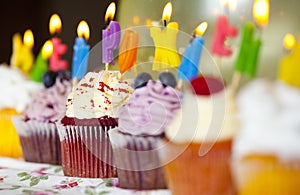 Colorful cupcakes with cream and fresh berries with burning candles