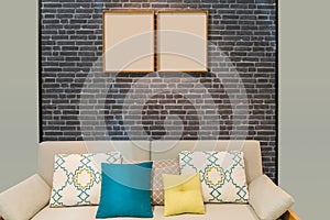 Colorful cushion pillows on modern beige color fabric sofa  with wooden picture frames on the grey brick wall interior for office