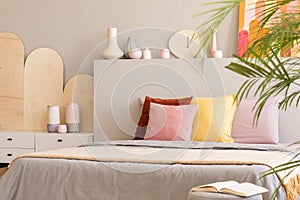 Colorful cushions on bed with headboard next to cabinet in grey