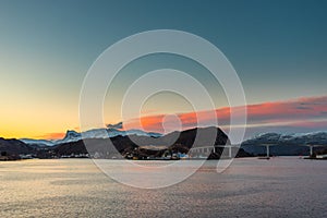 Colorful dawn over the coastline of Norway near the town Maloy with bridge, hills and snow capped mountains seen from cruise ship photo