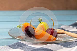 Colorful of deletable imitation fruits KANOM LOOK CHOUP is Thai snack put on a glass plate with a wooden spoon on a blue tablecl