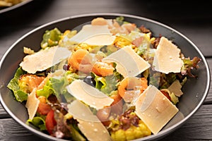 Colorful deliciously salad with salmon, Parmesan cheese, tomatoes and mixed greens on black plate. Close-up