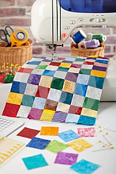 Colorful detail of quilt sewn from square pieces on sewing machine, quilting and sewing accessories