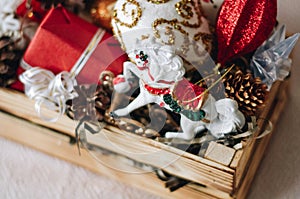 Colorful different Christmas toys and decor in the wooden gift box with horse, stars, cones, snowflake, snowman, gifts.