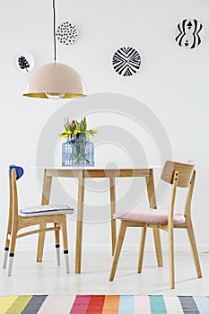 Colorful dining room interior with a table, chairs, striped rug, pastel chandelier and hanging plates on the wall