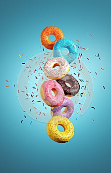 Colorful donuts flying with sprinkle explosion on blue background