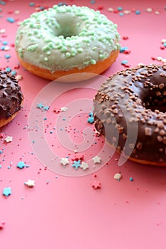 Colorful donuts in the glaze on the pink background with multi-colored sprinkles sugar stars