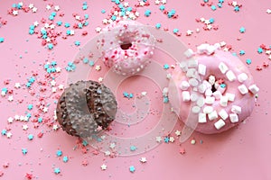 Colorful donuts in the glaze on the pink background with multi-colored sprinkles sugar stars