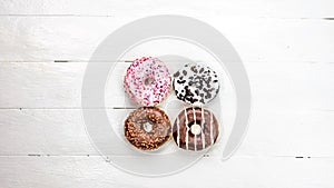 Colorful donuts on white wooden table. Sweet icing sugar food with glazed sprinkles, doughnut with frosting. Top view with copy