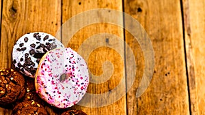 Colorful donuts on wooden table. Sweet icing sugar food with glazed sprinkles, doughnut with chocolate frosting. Top view with