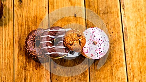 Colorful donuts on wooden table. Sweet icing sugar food with glazed sprinkles, doughnut with chocolate frosting. Top view with